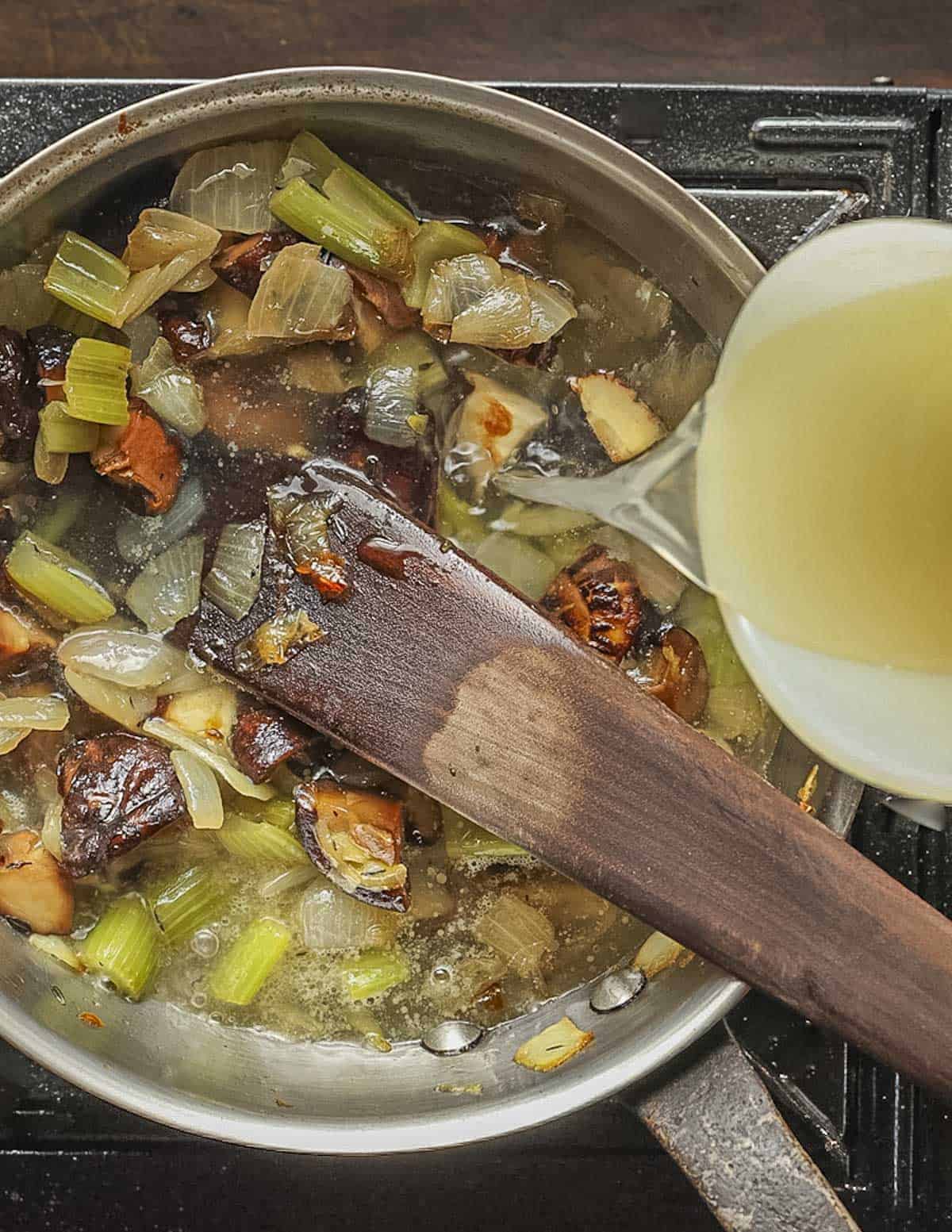 Adding chicken stock to a pot of roasted shiitake mushrooms and vegetables. 
