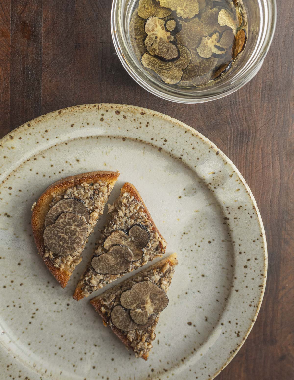 A piece of toast with tartufata truffle spread next to a jar of truffle slices in oil. 