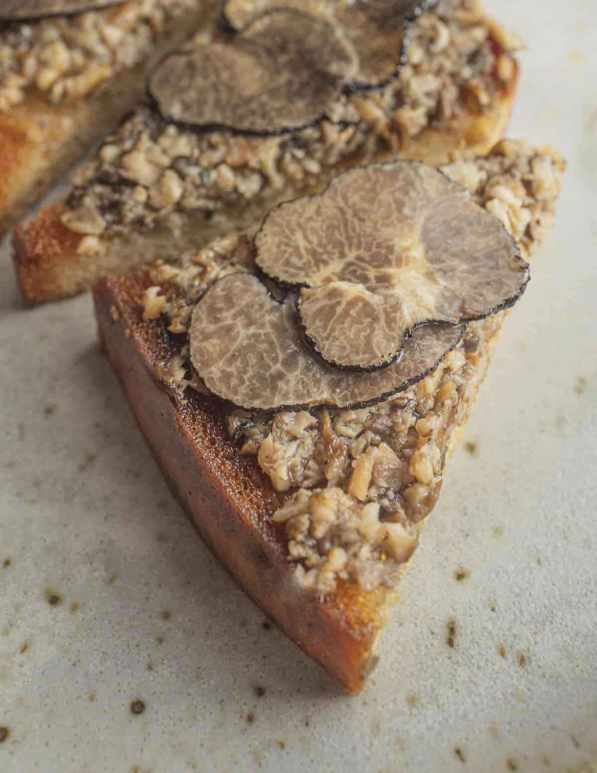 Mushroom tartufata spread on a piece of toast topped with preserved truffle slices in oil. 