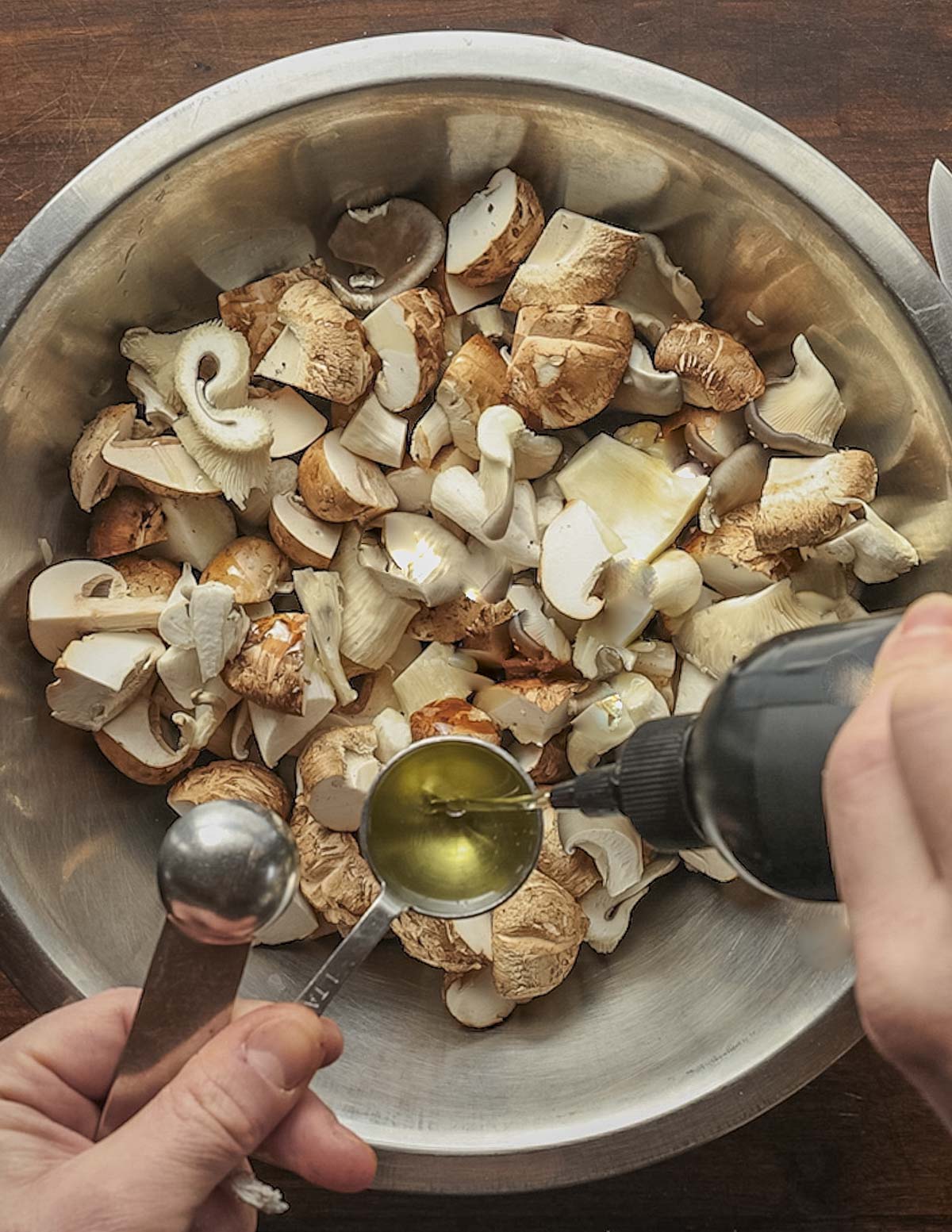 Tossing a bowl of cut mushrooms with cooking oil. 