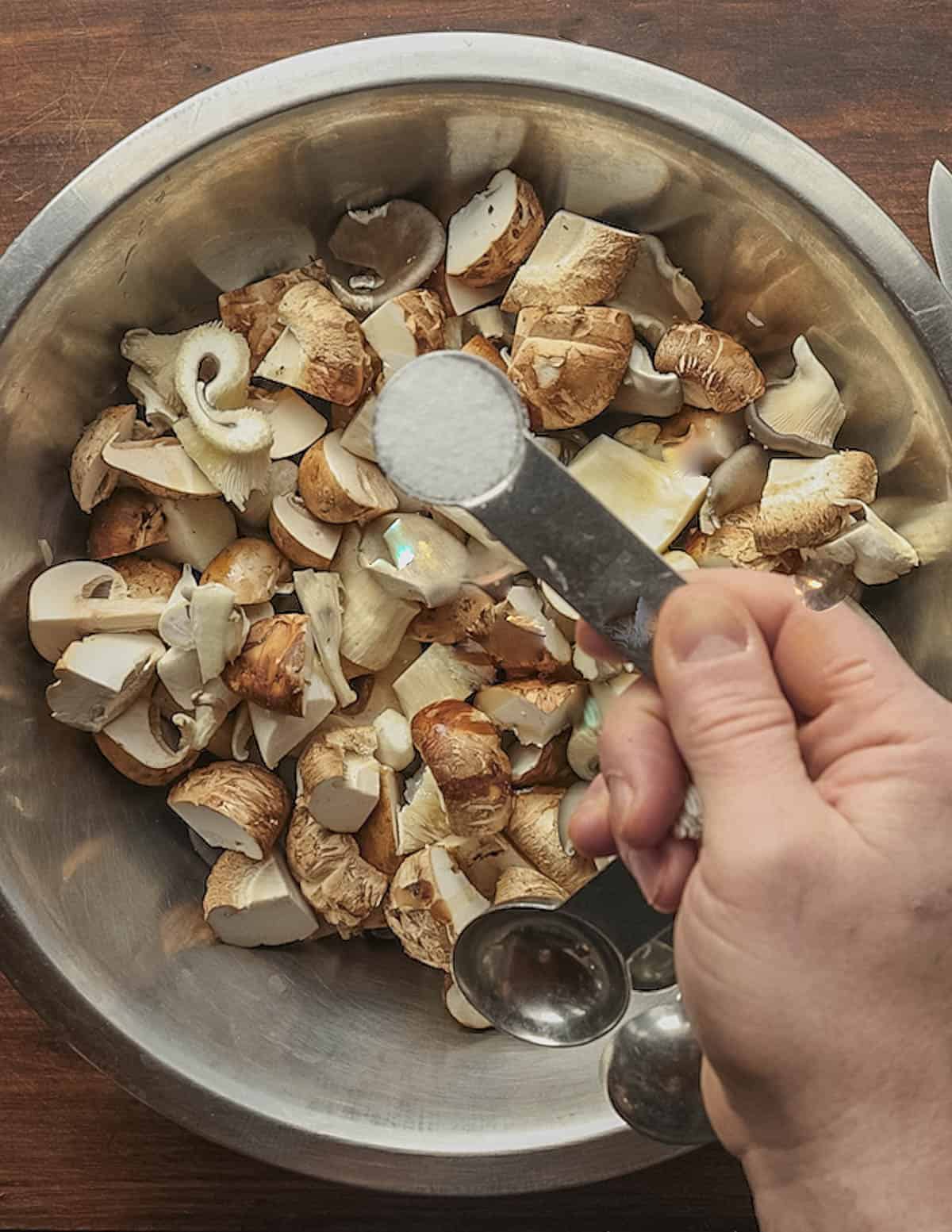 Seasoning a bowl of oiled mushrooms with salt. 