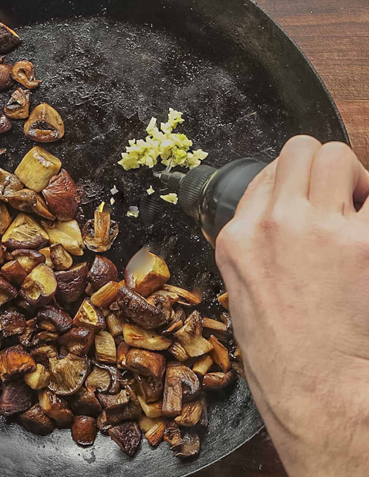 Adding garlic to a pan of roasted mushrooms. 