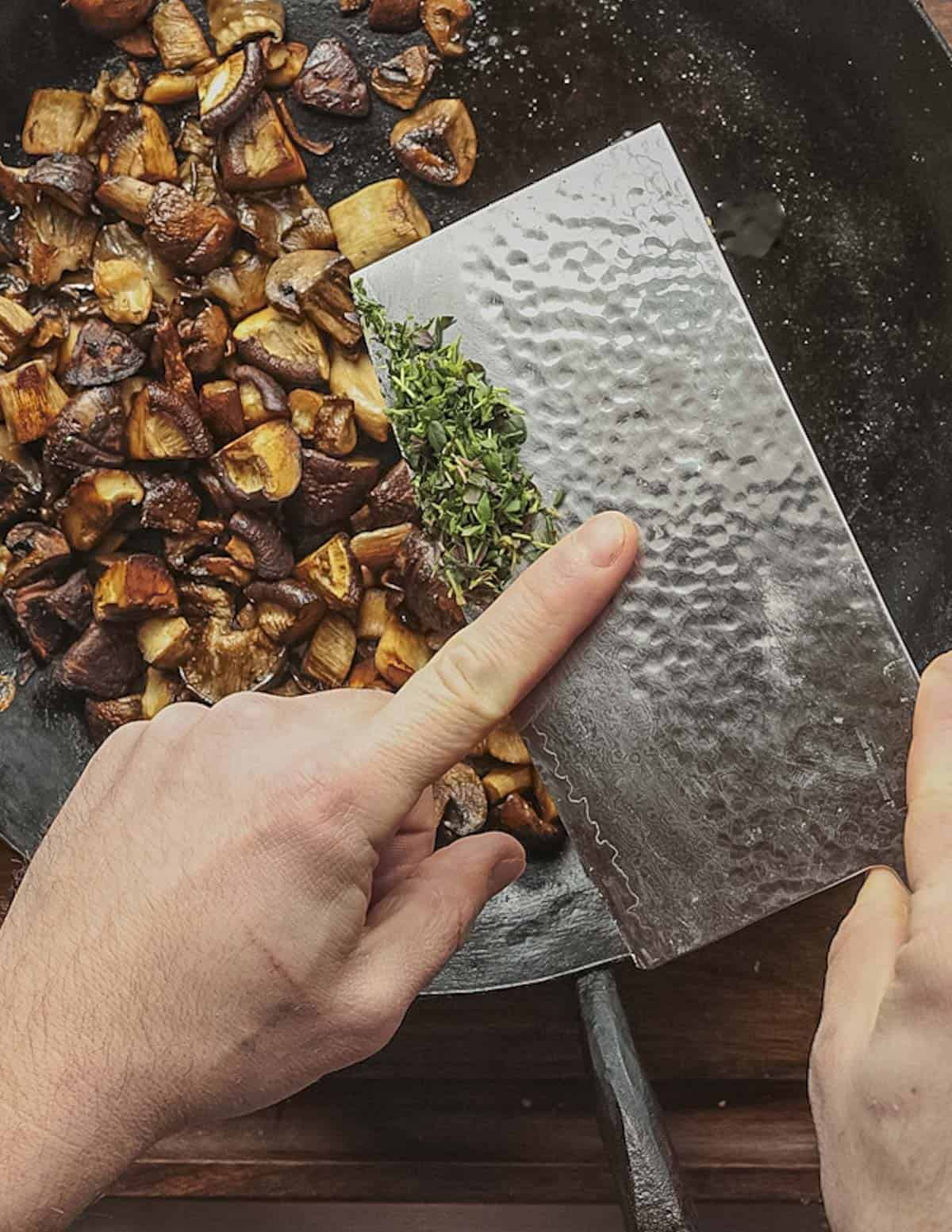 Adding chopped fresh thyme leaves to a pan of roasted mushrooms. 