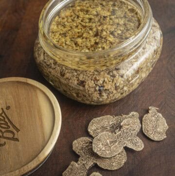 A jar of tartufata truffle sauce next to sliced fresh Bianchetto truffles and a knife.