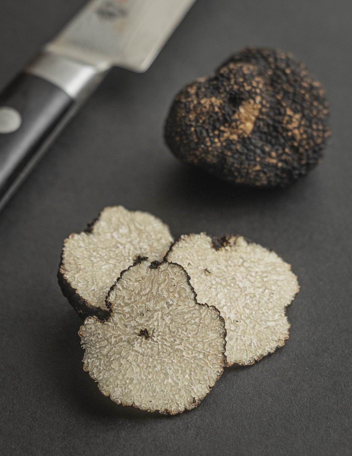 Fresh summer truffles (Tuber aestivum) slices next to whole fresh truffles and a knife. 