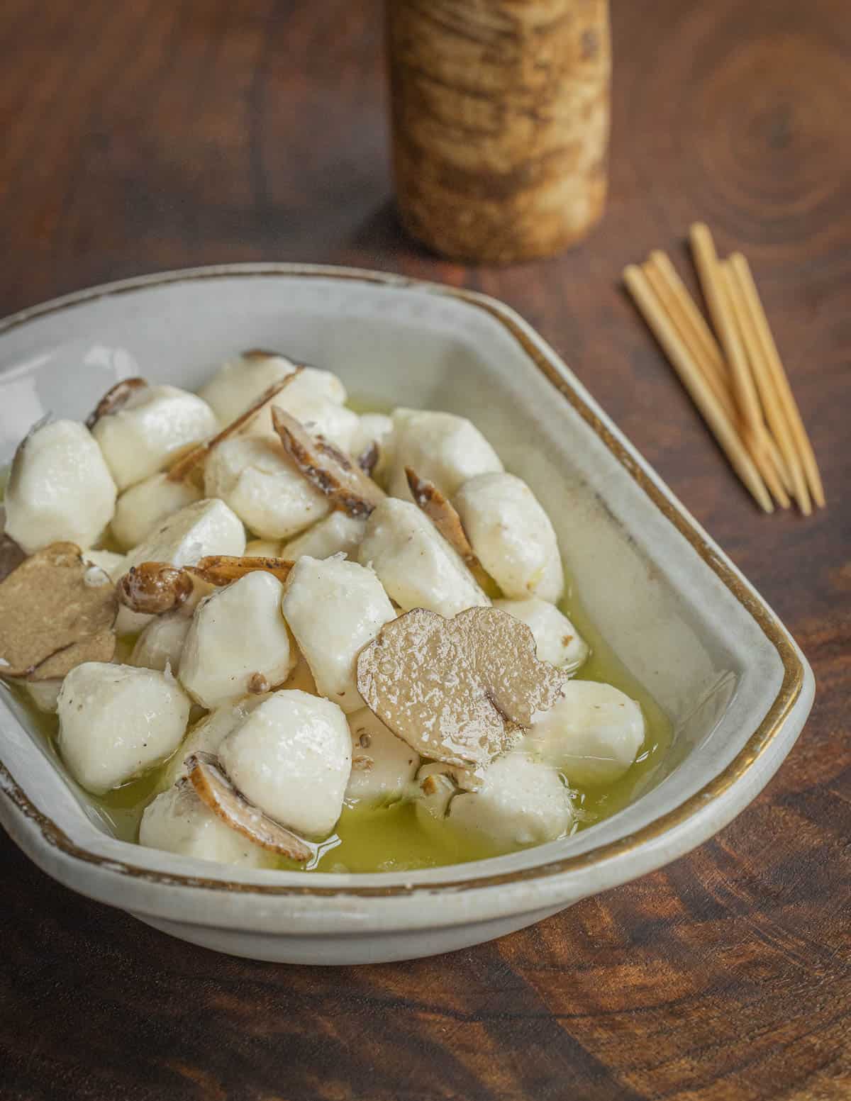 A small dish of mozzarella balls with pecan truffle slices and pecan truffle oil.