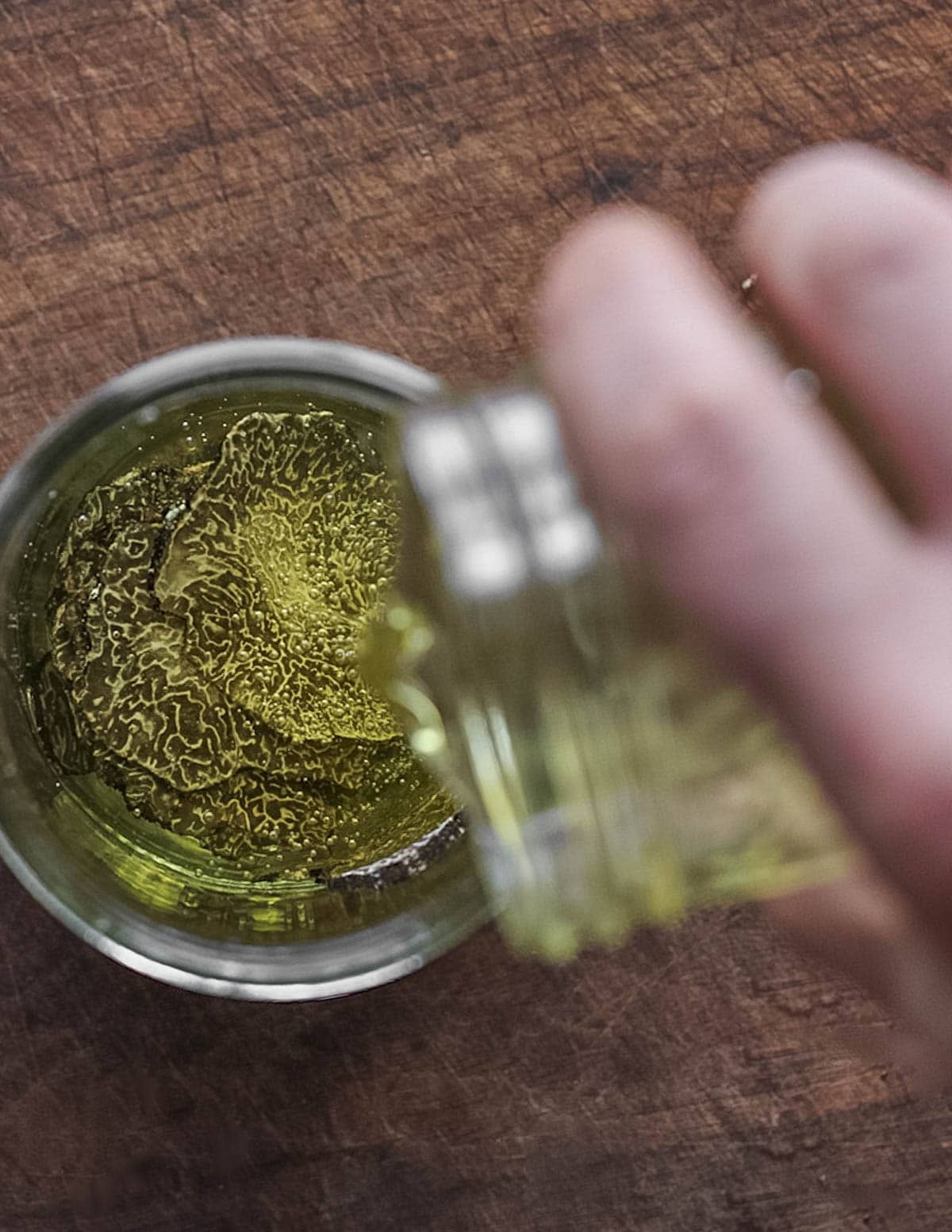 Pouring grapeseed oil over a jar of salted truffle slices. 