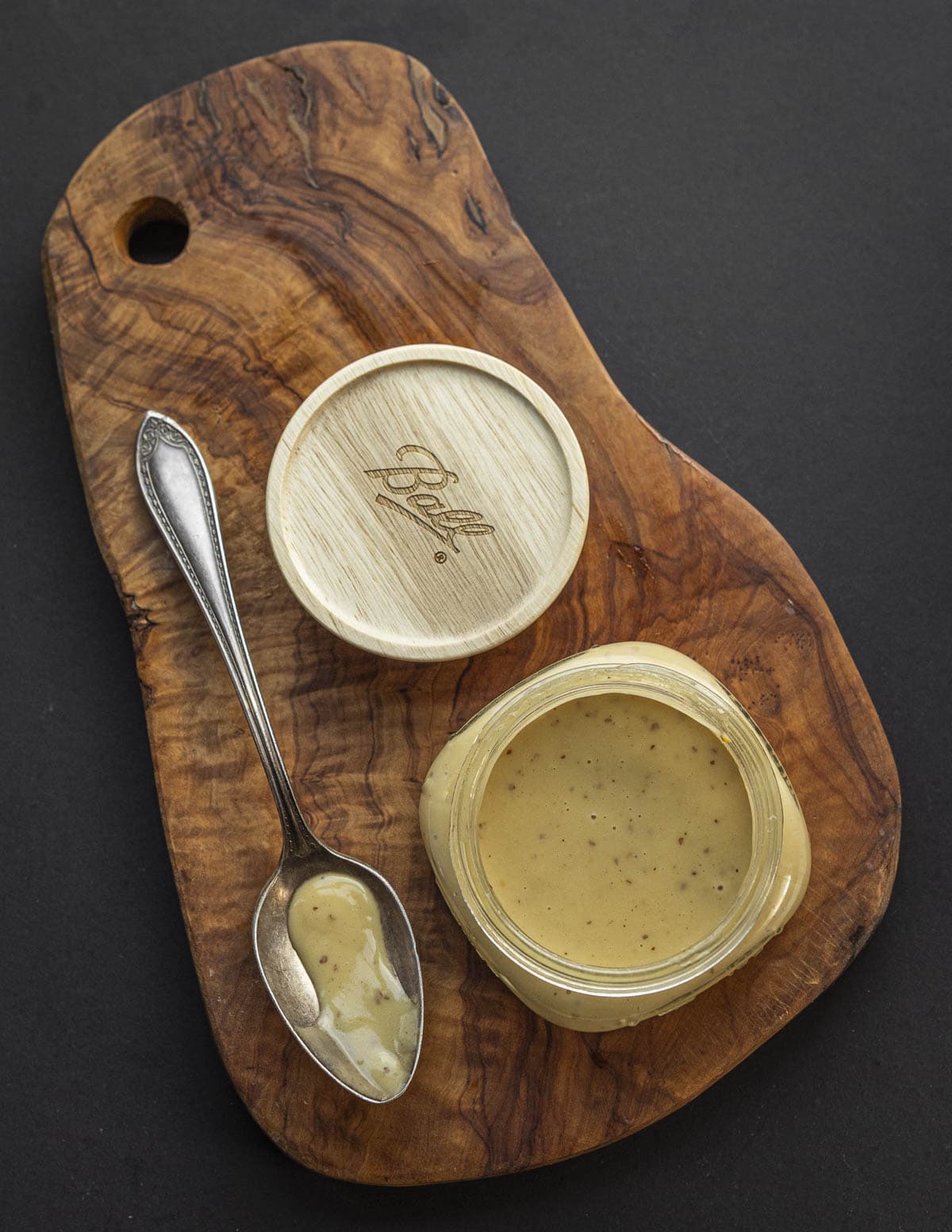 A jar of dijon maple vinaigrette in a mason jar next to a spoon on an olive wood background.