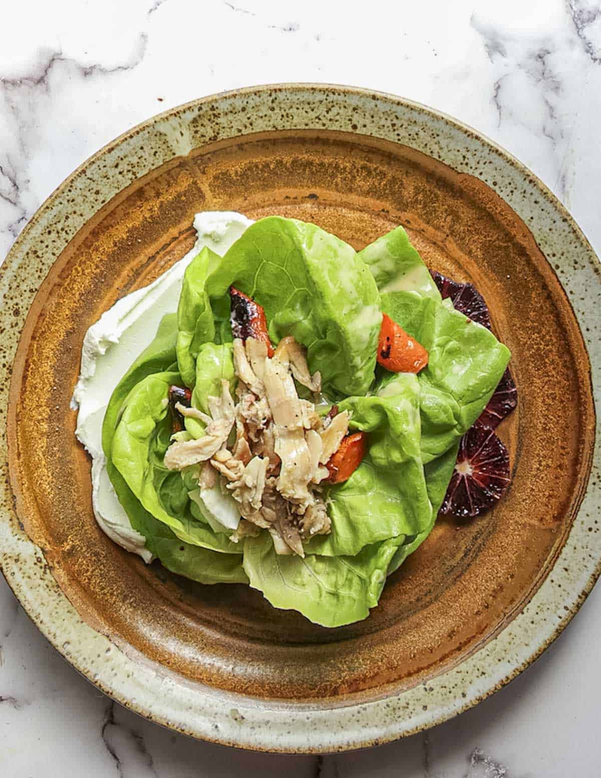 Topping butter lettuce salad with roasted chicken, herbs and roasted vegetables. 