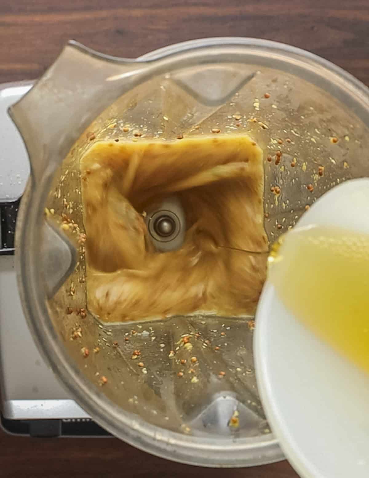 Drizzling in olive oil into a blender to make dijon maple dressing. 