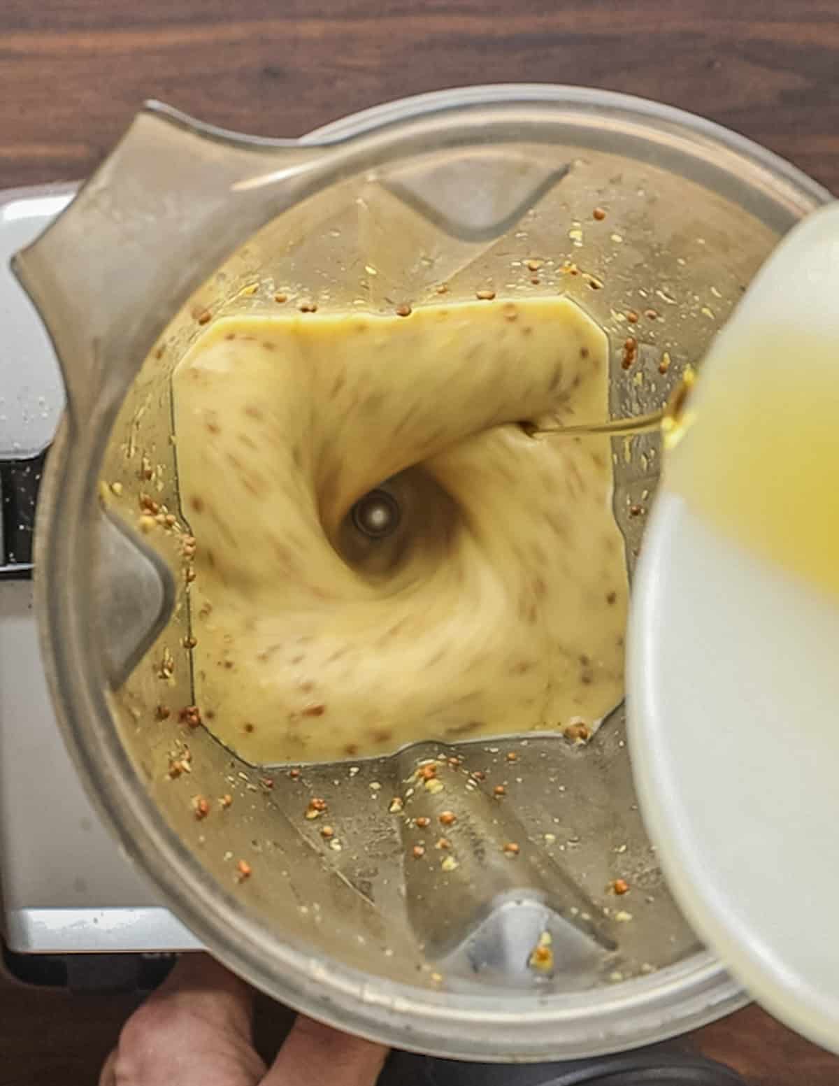 Drizzling in oil in a thin stream into a blender. 