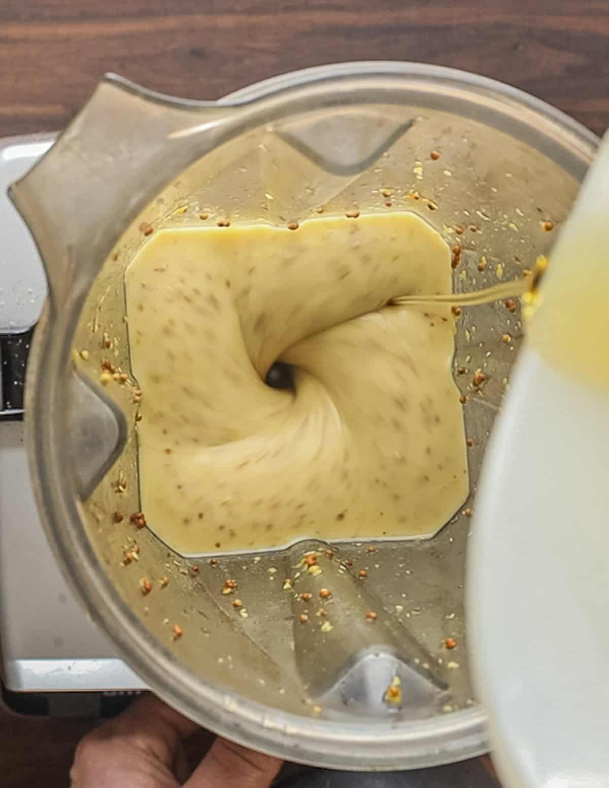 A top down view of a blender drizzling in oil to make a thick, creamy dressing. 