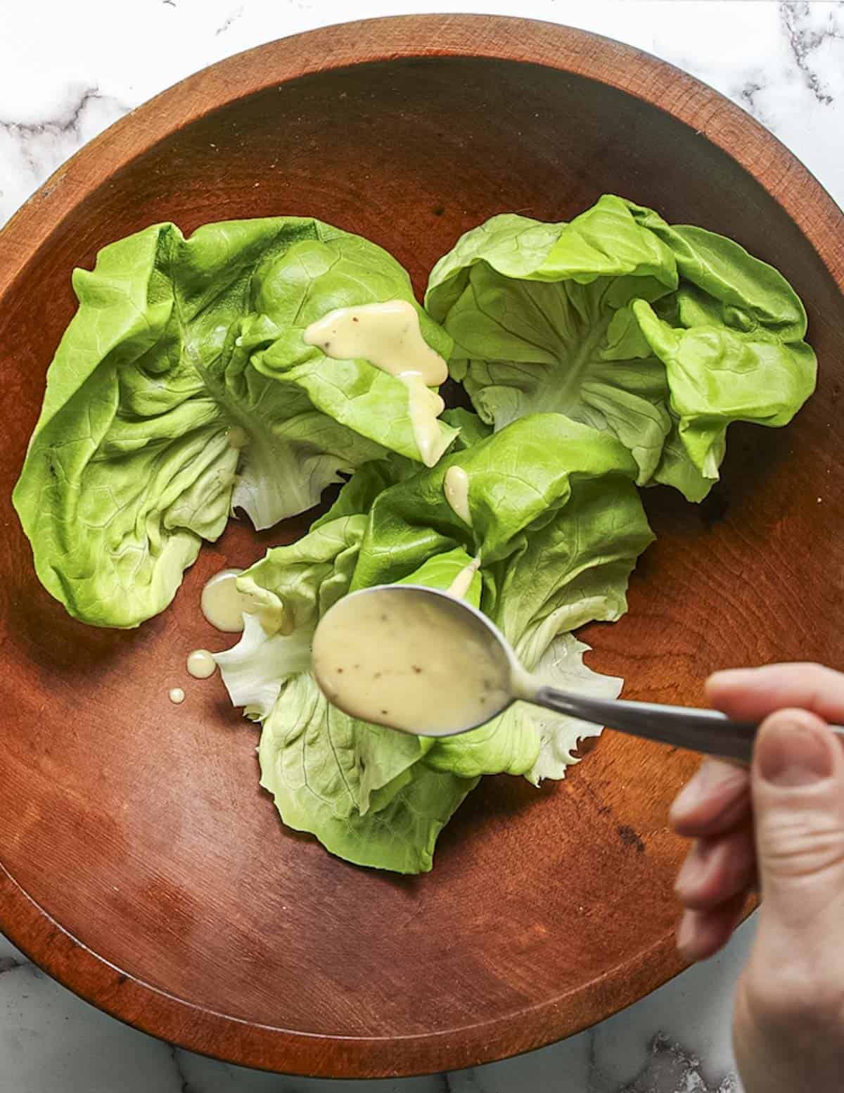 Pouring maple vinaigrette over fresh butter lettuce leaves. 