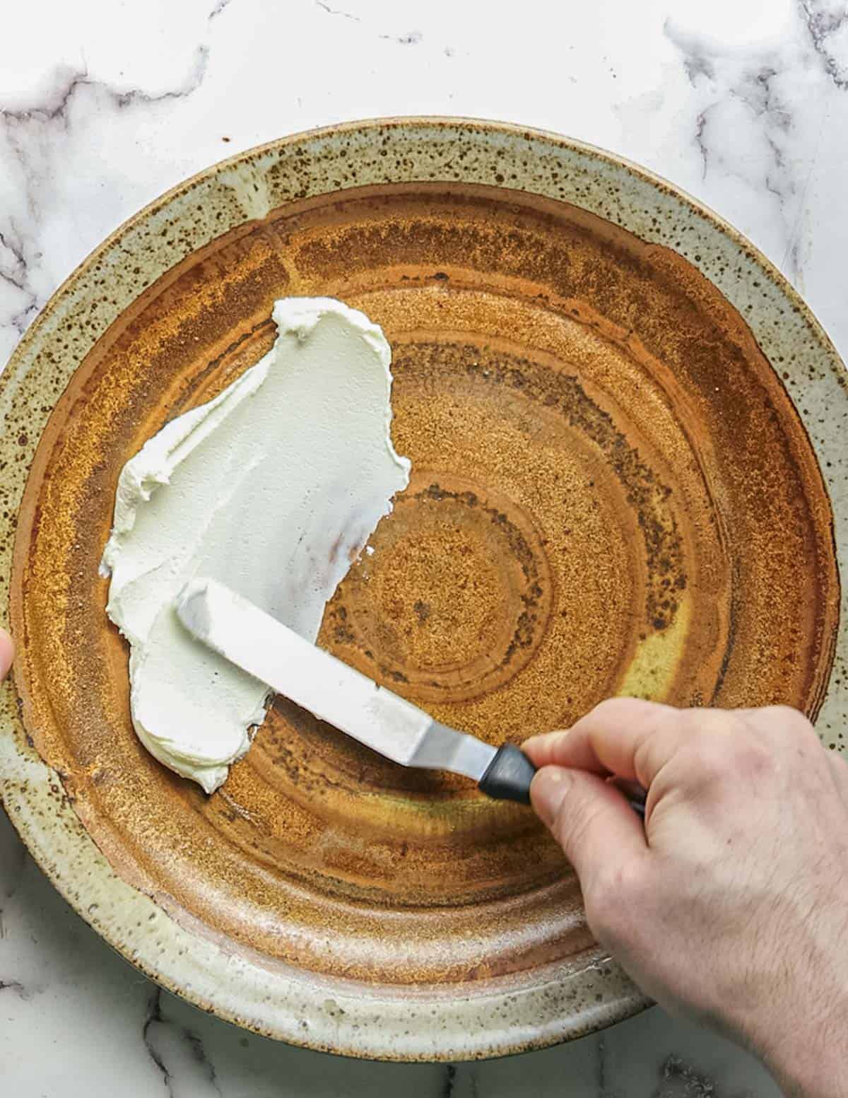 Spreading goat cheese on a plate with an offset spatula for a salad. 