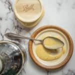 A dish of maple dressing next to a bottle of maple syrup.