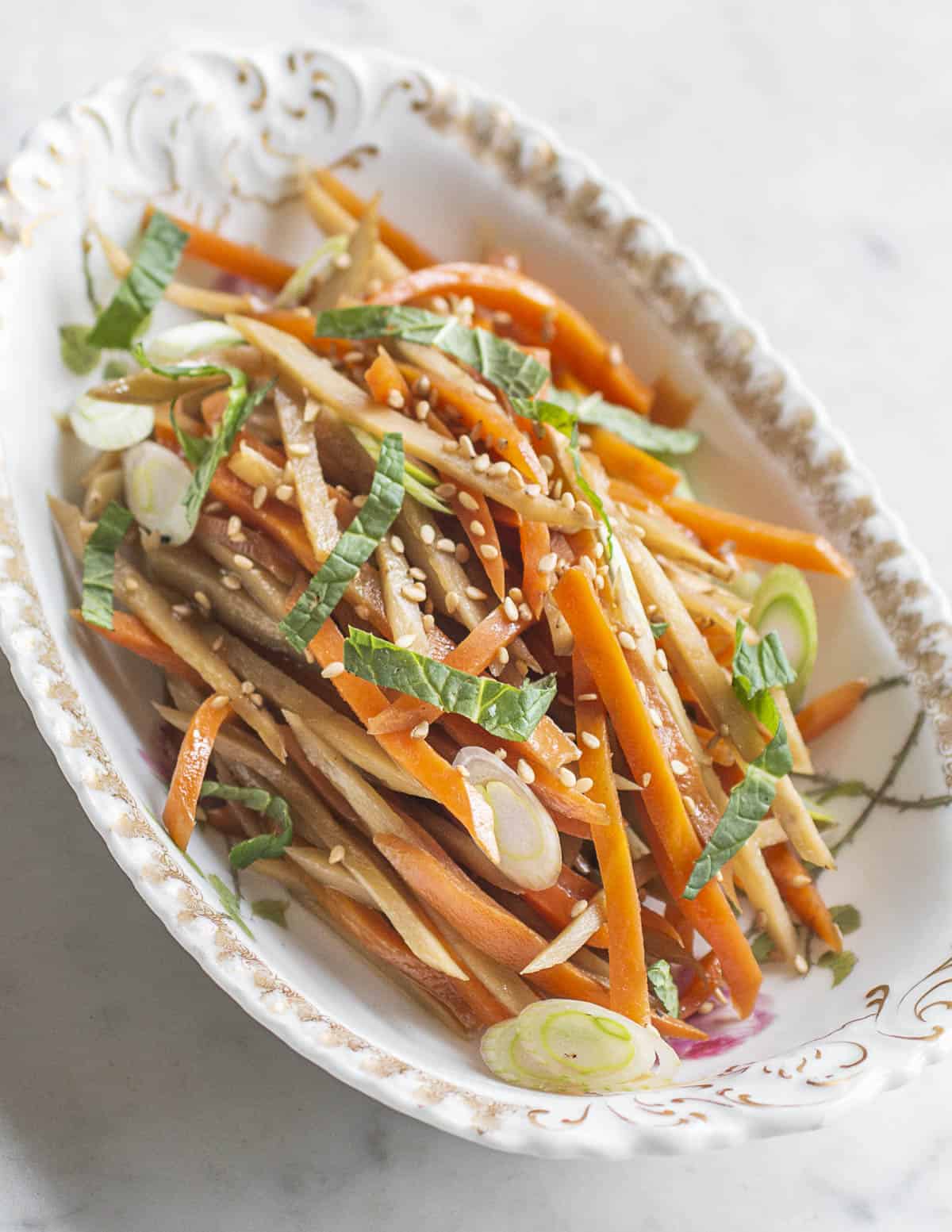 Kinpira gobo burdock recipe with carrots in a dish garnished with sesame seeds mint and scallions. 