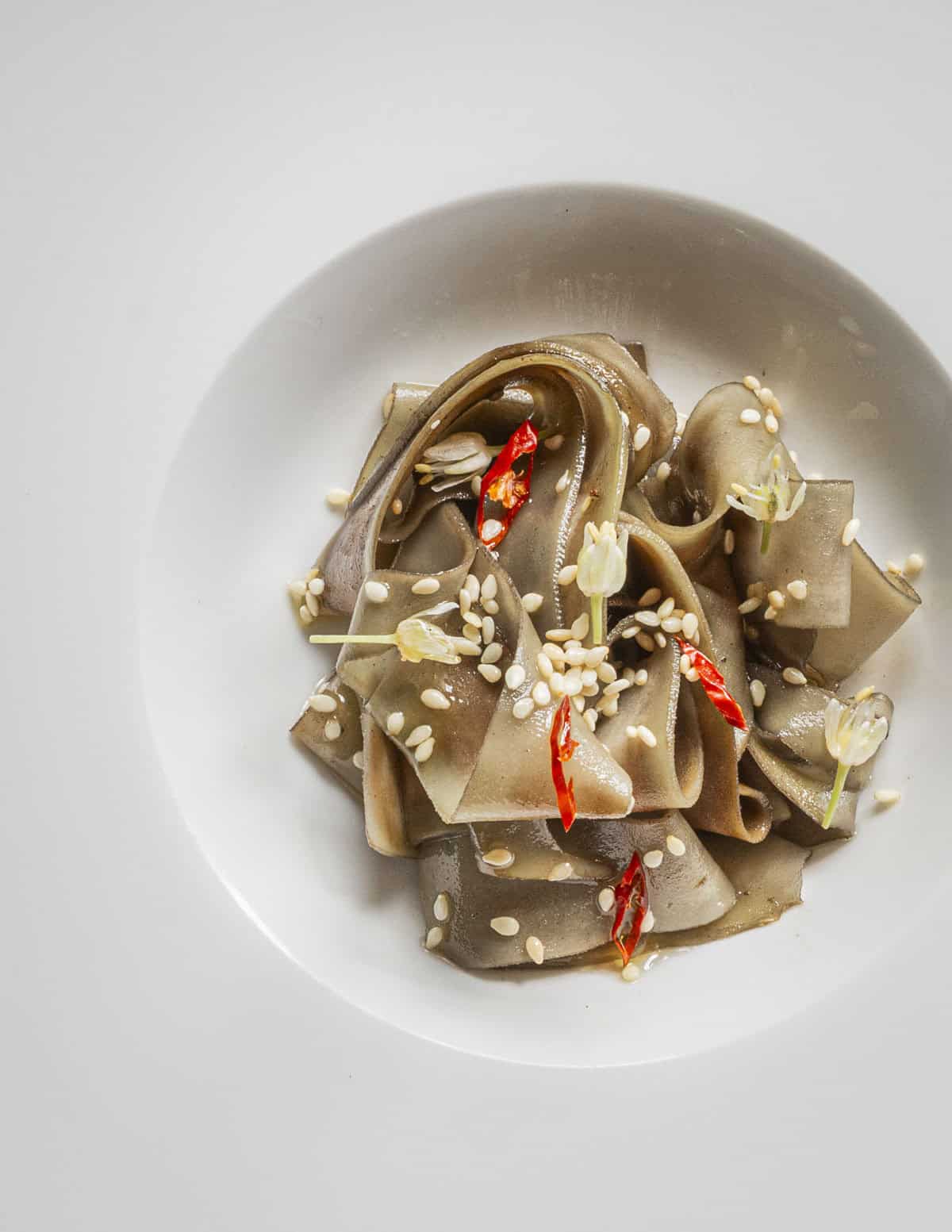 Stir-fried burdock stem noodles with thai chili, ramp flowers and sesame oil. 