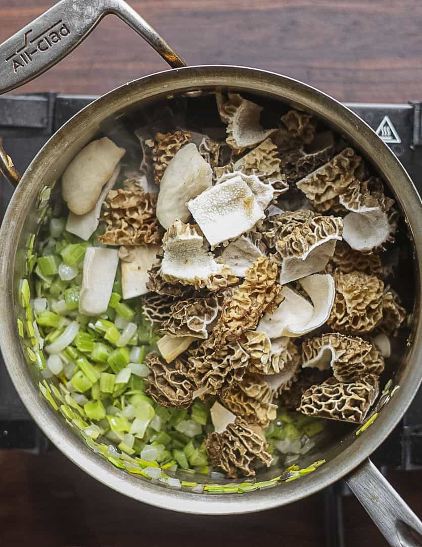 Adding cut up morel mushrooms to a pan of celery, onion and leek to make morel soup. 