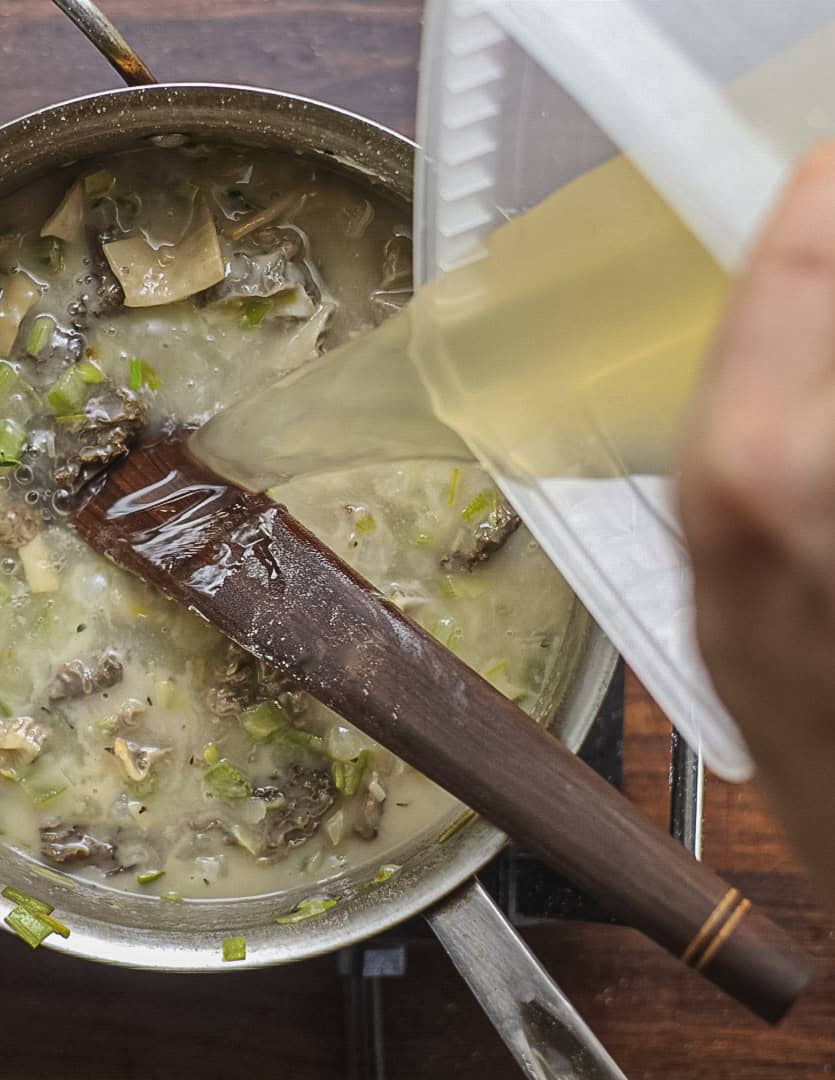 Adding the rest of the chicken stock to a pot of morel mushroom soup.  