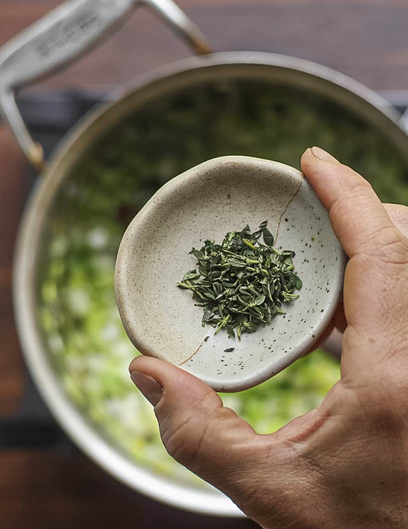 Adding a pinch of chopped fresh thyme leaves to a pan of celery, onion and leek. 
