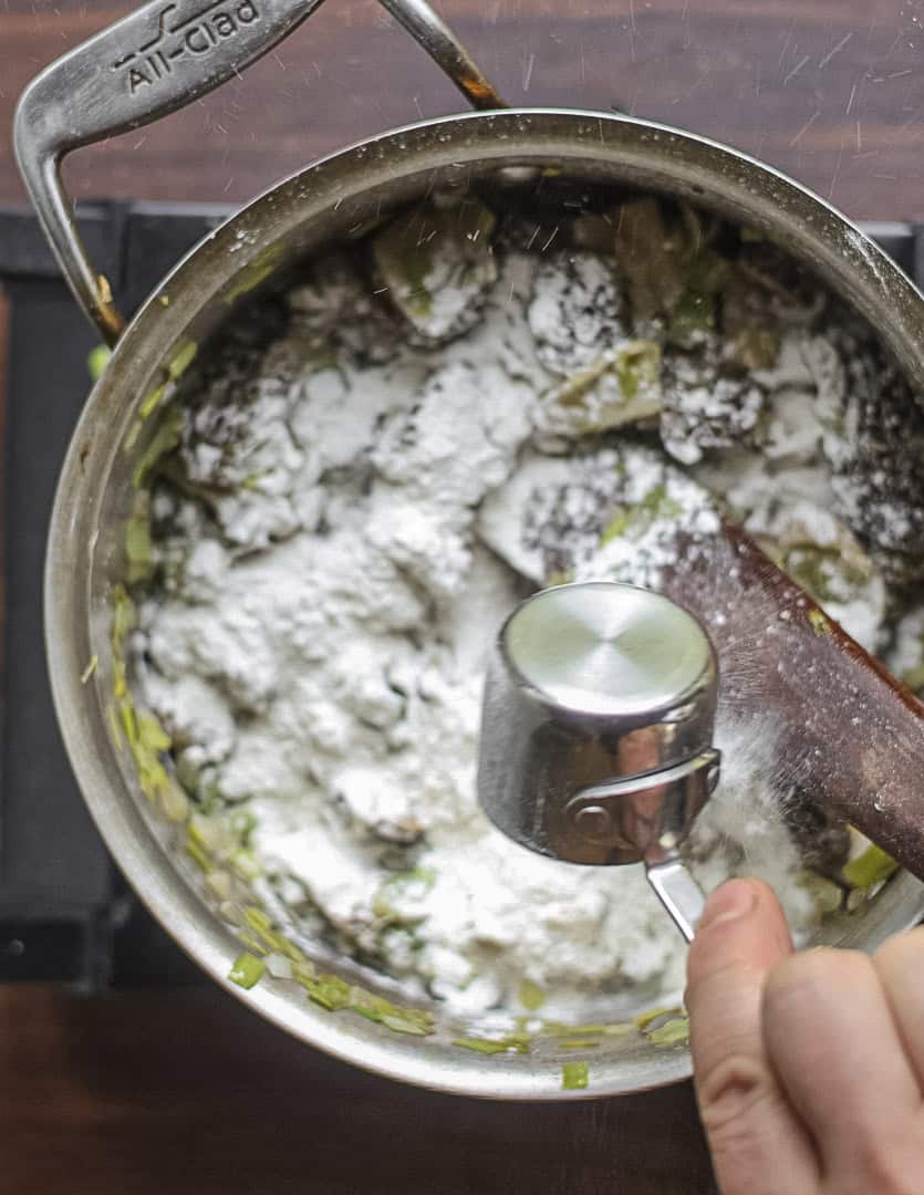 Adding all purpose flour to a pan of morel mushrooms and vegetables. 