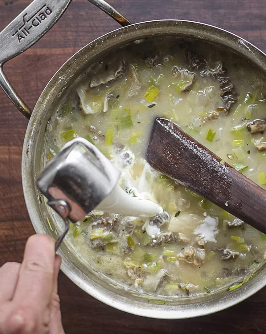 Adding heavy cream to a pot of cream of morel mushroom soup. 