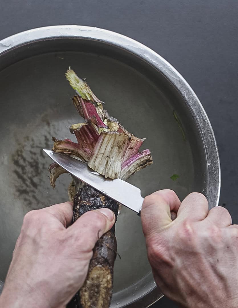 Trimming the top portion from a burdock root using a knife. 