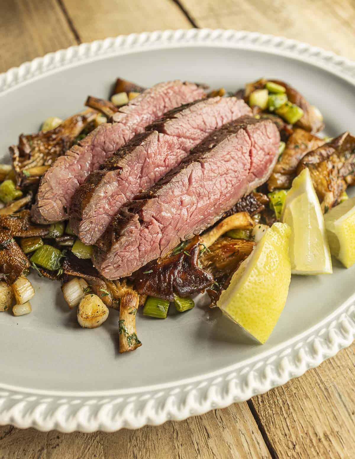 Sliced grilled flank steak with golden oyster mushrooms and green garlic. 