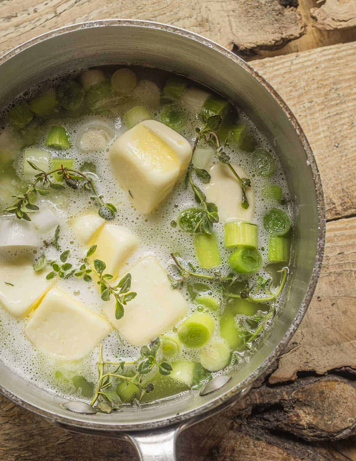 Cooking sliced green garlic in butter with fresh thyme in a small pan to make garlic confit. 