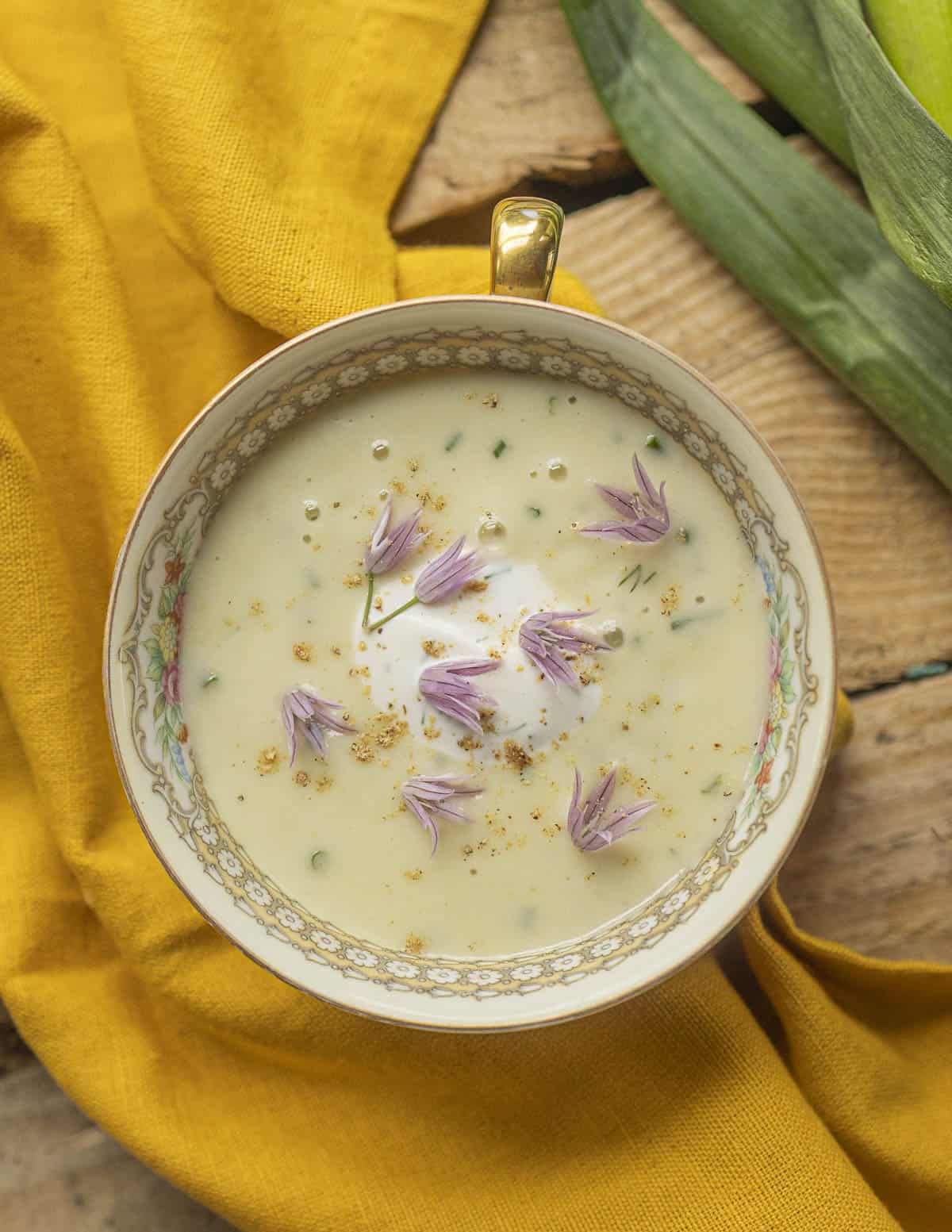 Green garlic soup in a china tea cup garnished with sour cream, chive flowers and white pepper. 