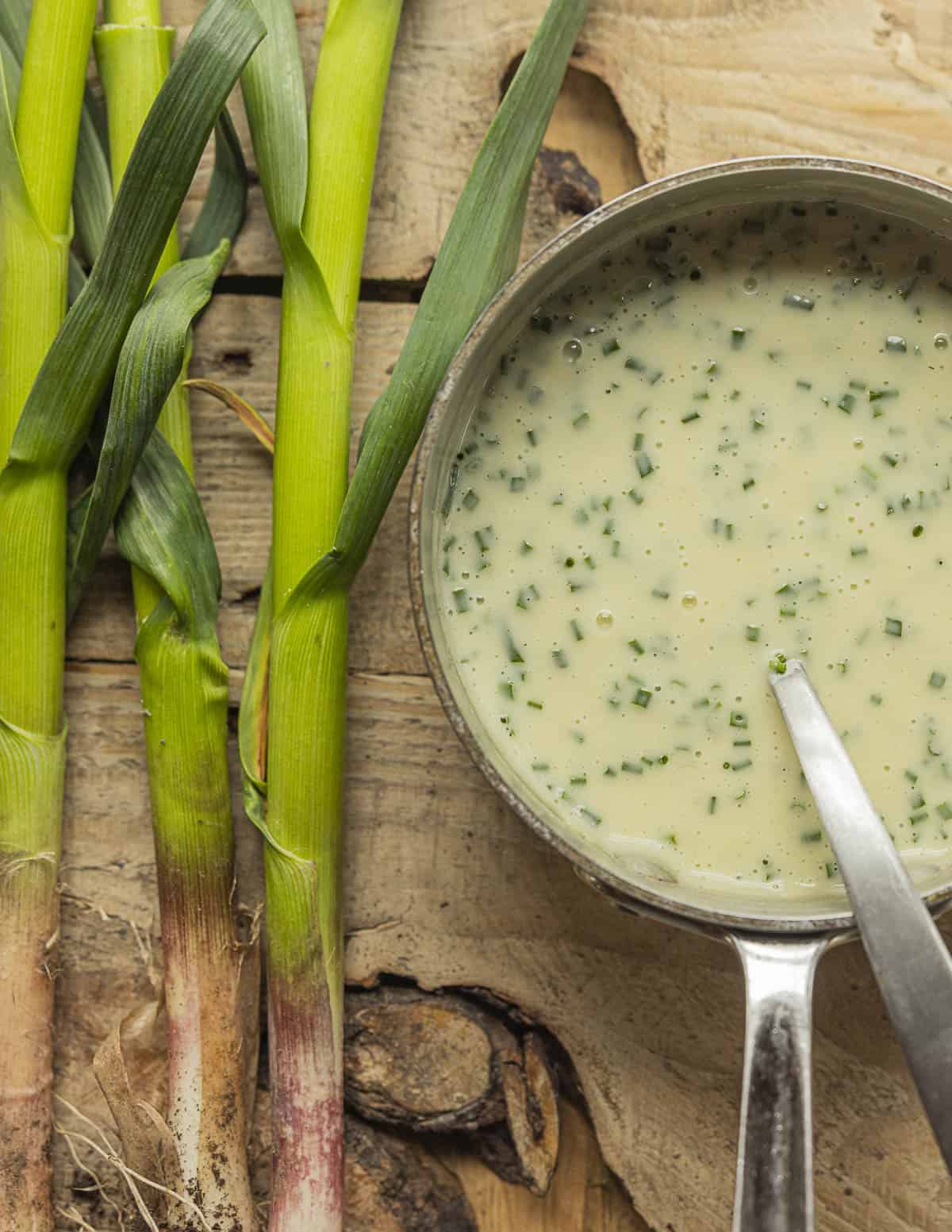 Green garlic soup with chives in a pan next to fresh stalks of heirloom green garlic. 