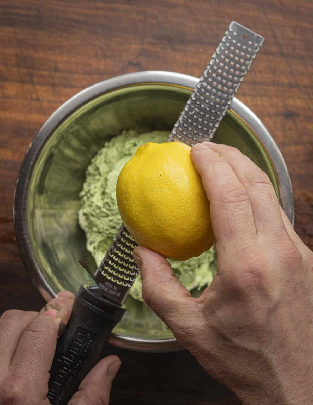 Zesting a lemon over a bowl of ramp cream cheese. 