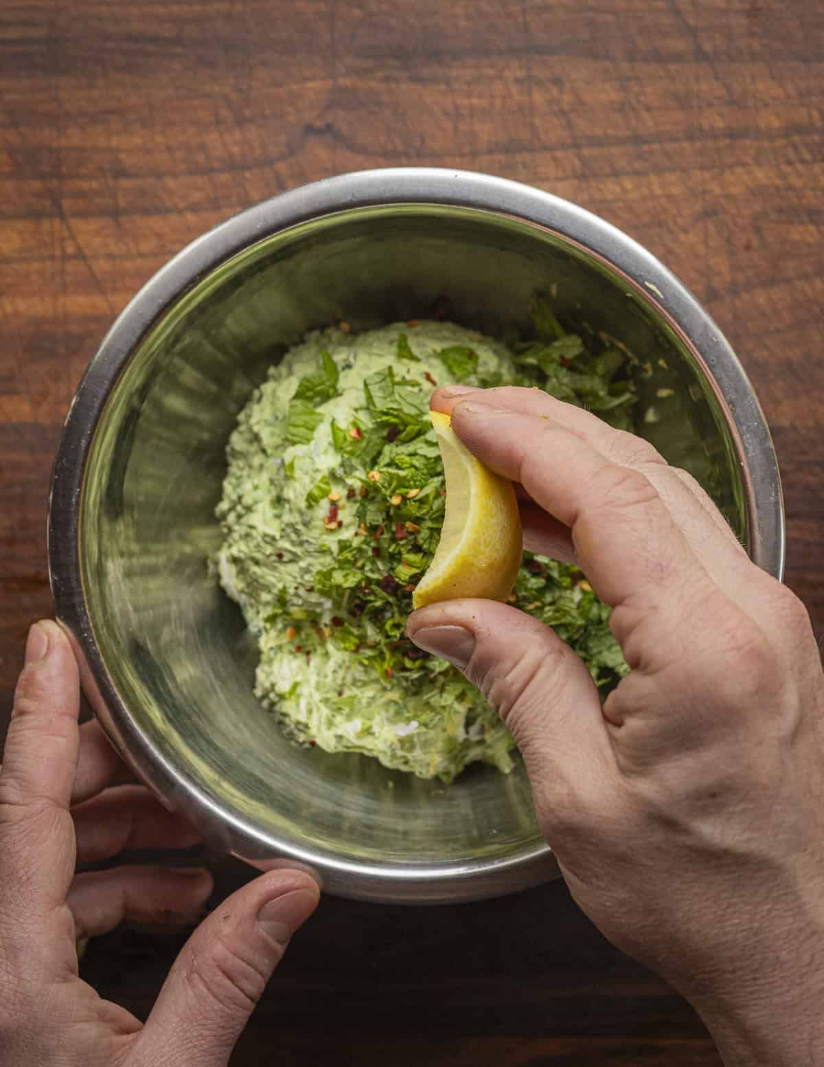 A hand squeezing fresh lemon juice onto a bowl of ramp leaf cream cheese. 