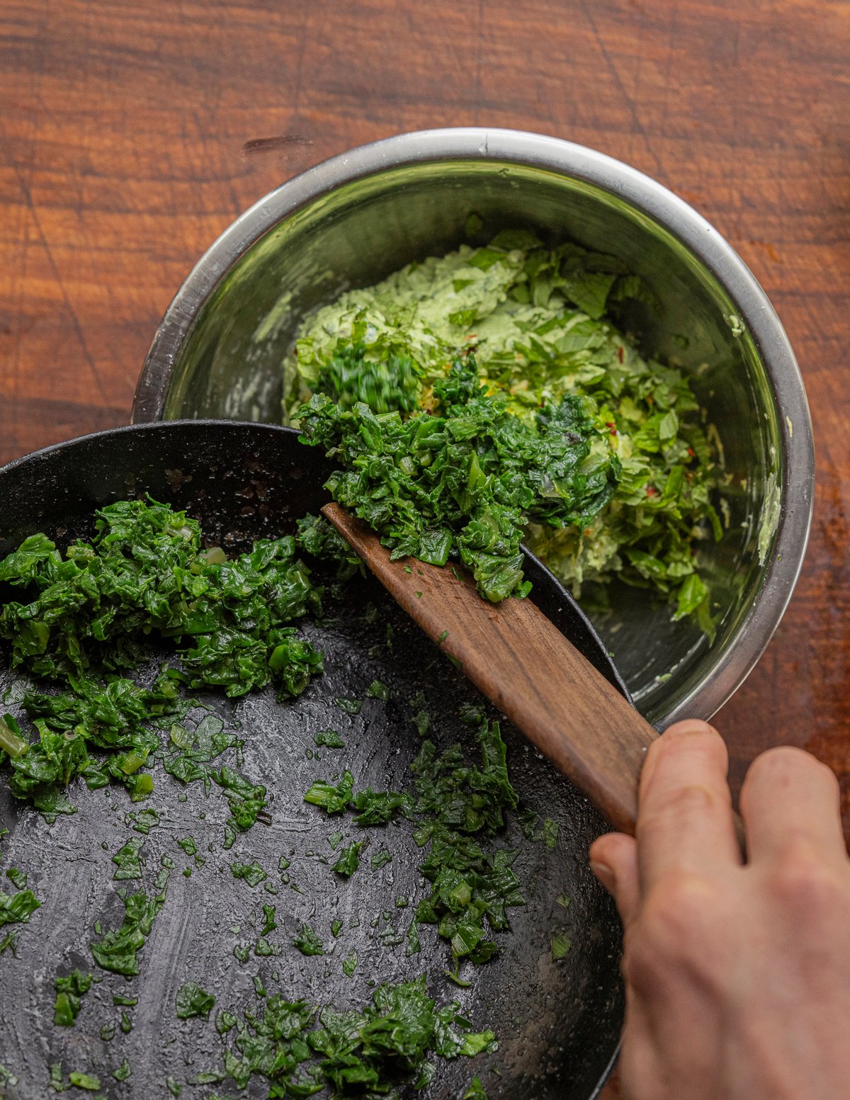 Mixing cooked ramp leaves into a bowl of green cream cheese. 