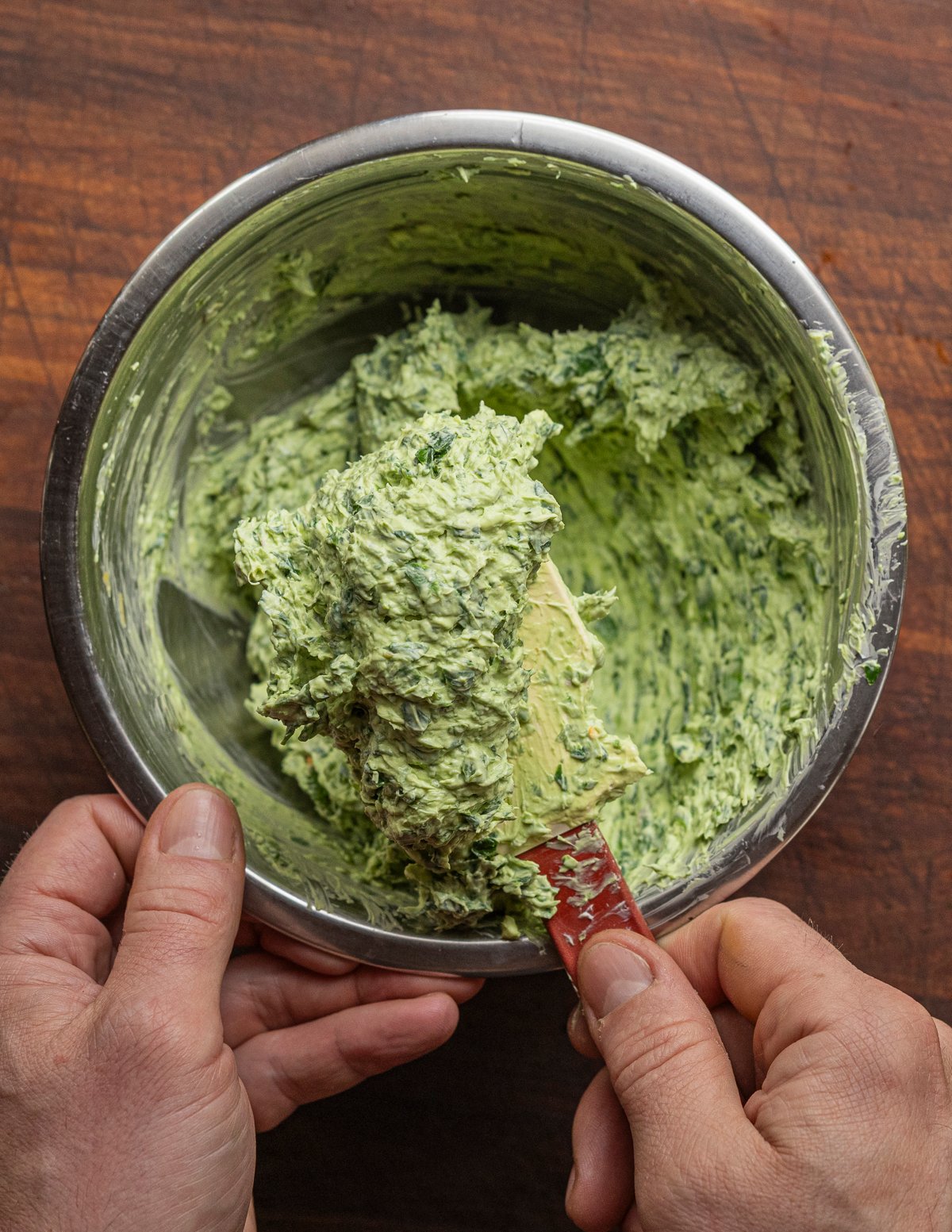 Folding and mixing green ramp cream cheese with a spatula in a bowl. 