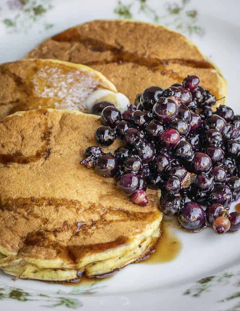 A plate of yellow cattail pollen pancakes with maple syrup and wild blueberries. 