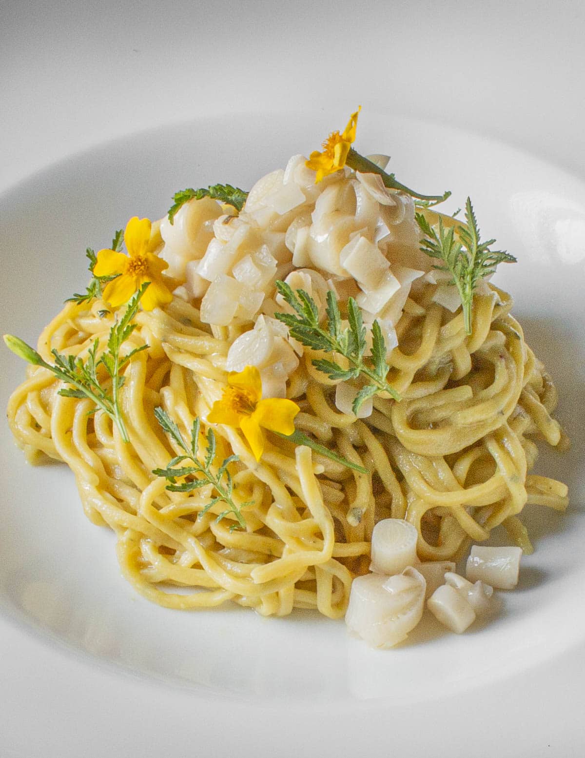 A bowl of duck egg pasta with cattail pollen butter sauce topped with cattail shoot relish and signet marigolds. 
