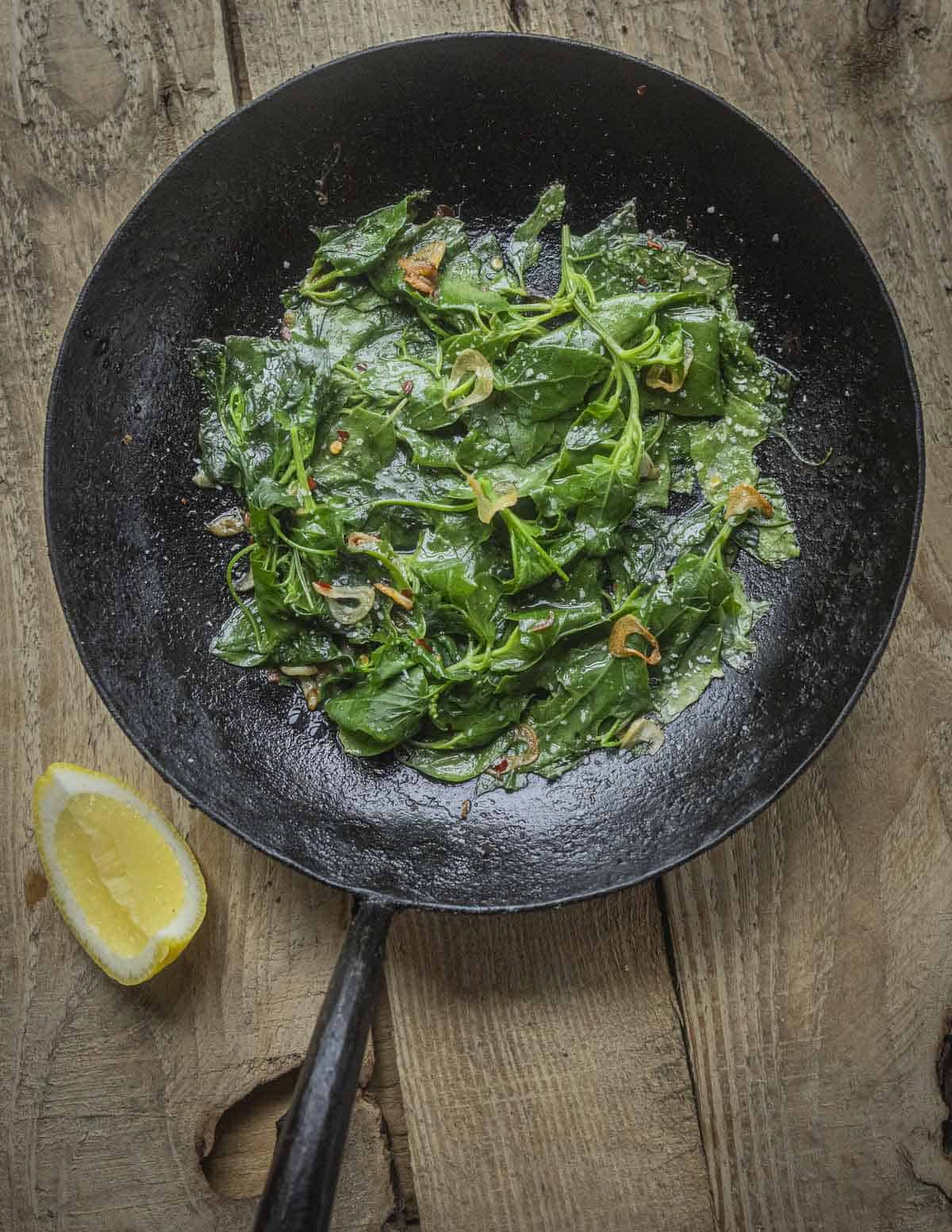 A carbon steel pan filled with foraged lambsquarters, wild green orache, garlic and hot pepper flakes. 