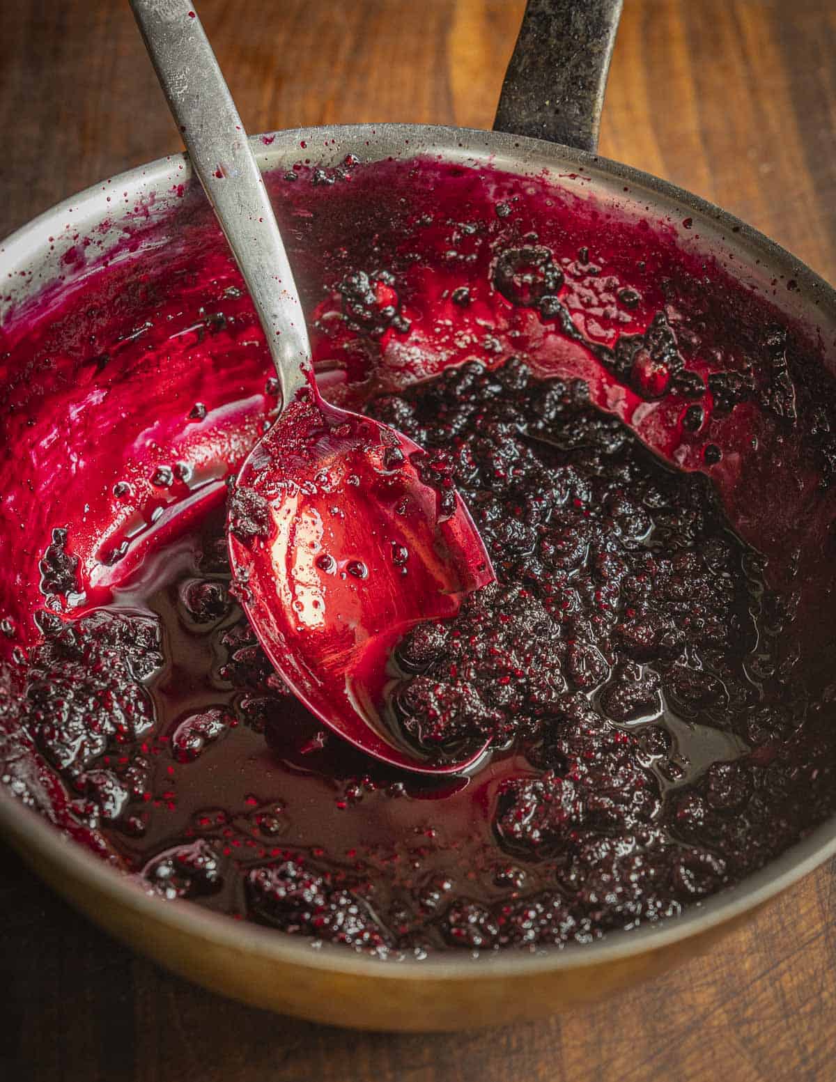 Black raspberry preserves or jam in a pan showing cooked fruit and a deep red color. 