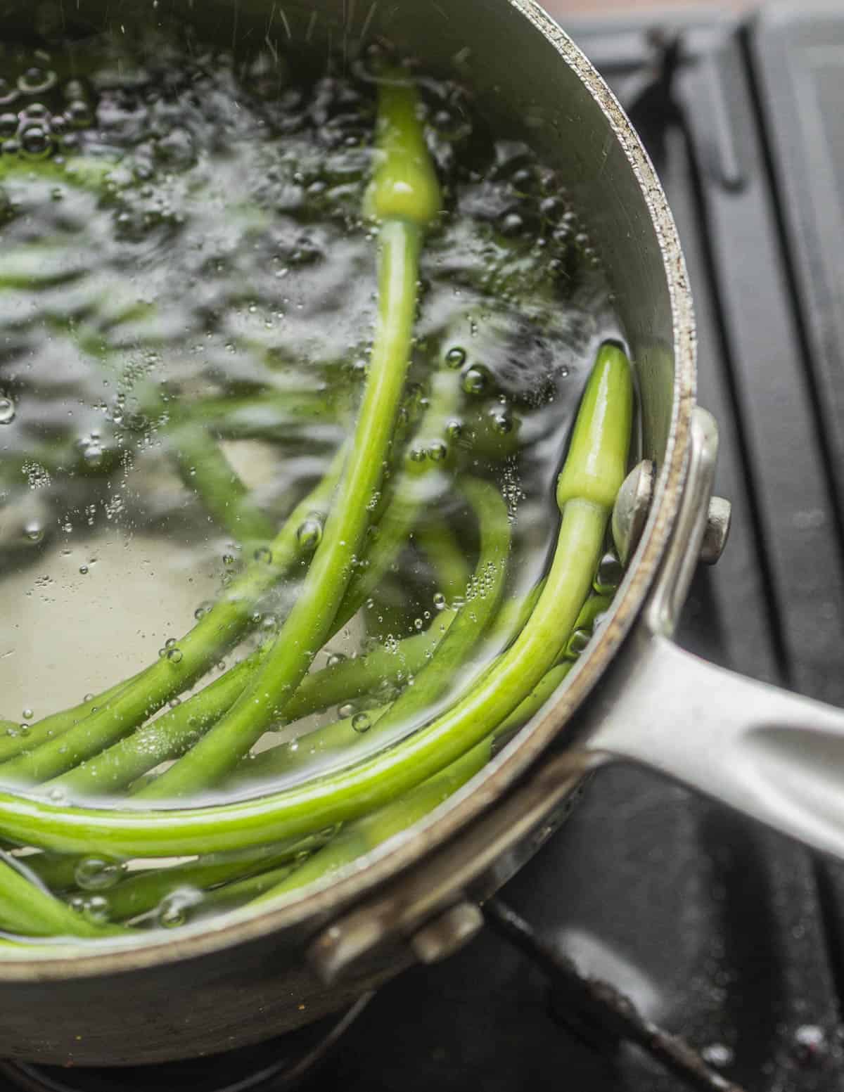 Garlic scapes being blanched in a pot of boiling water before grilling.