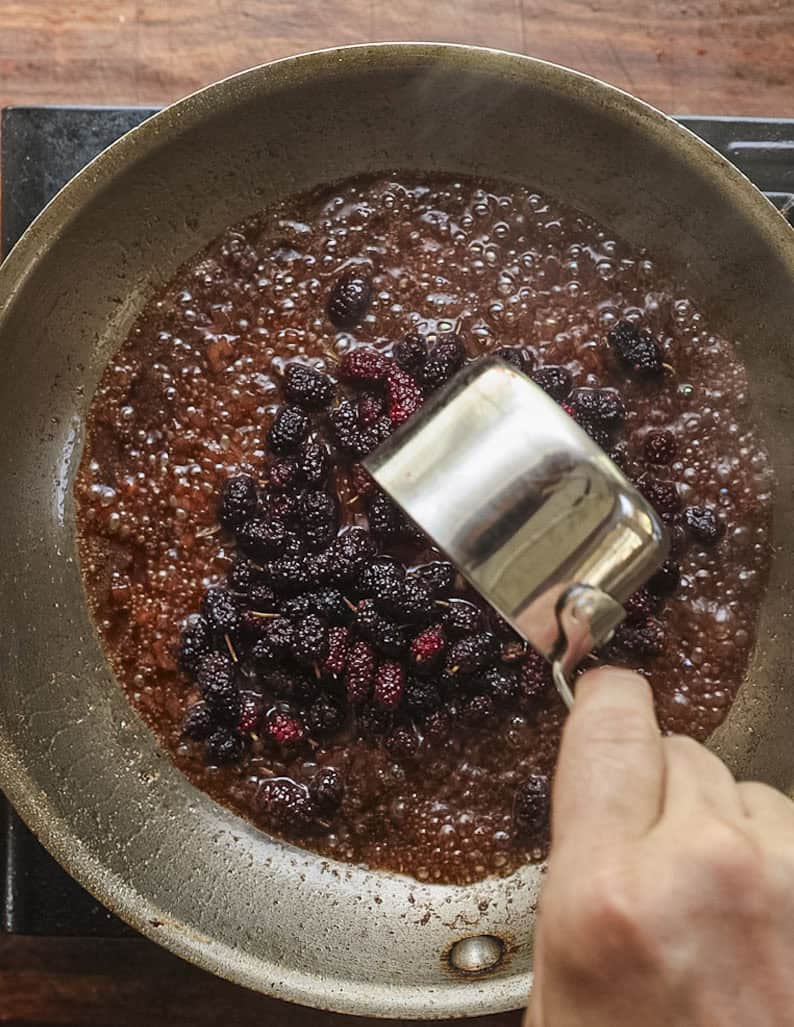 Adding mulberries to a pan of vinegar and shallots. 