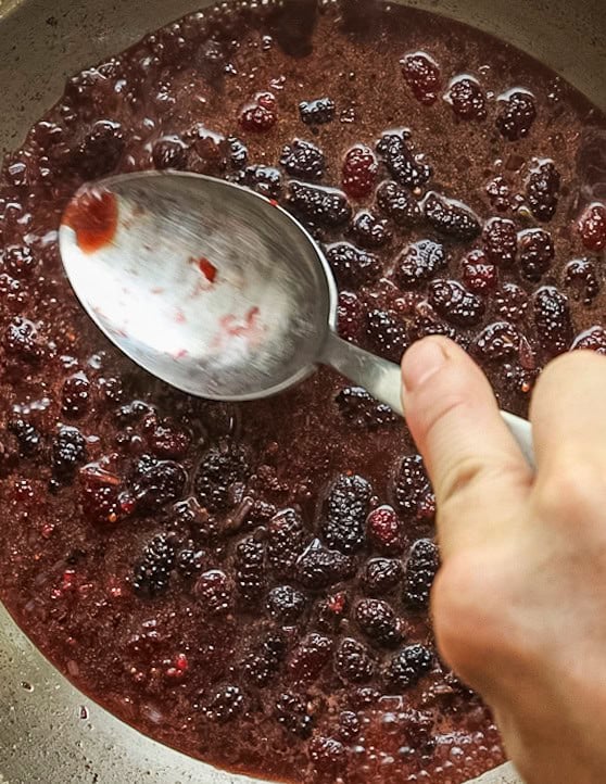 Crushing mulberries in a pan with the back of a spoon. 