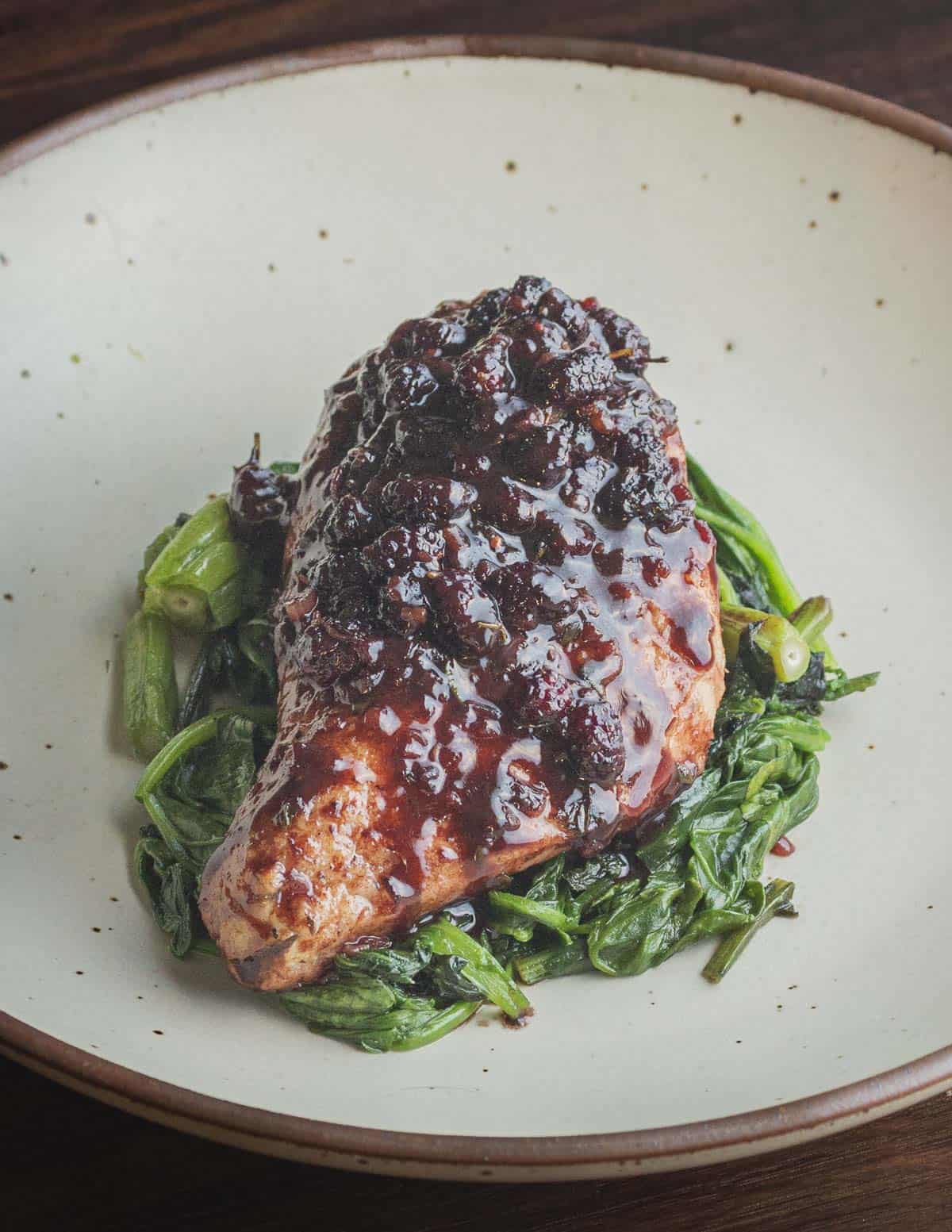 A boneless skinless chicken breast topped with mulberry sauce served on buttered wild lettuce greens. 
