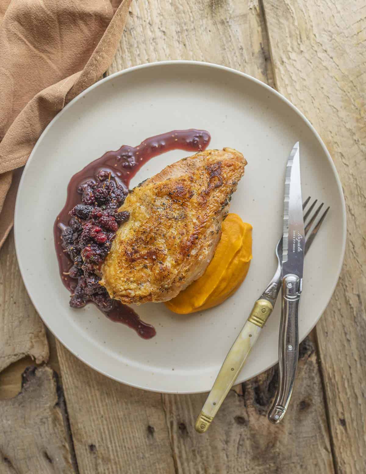 A golden brown skin on chicken breast surrounded by mulberry sauce and orange carrot puree on a plate. 