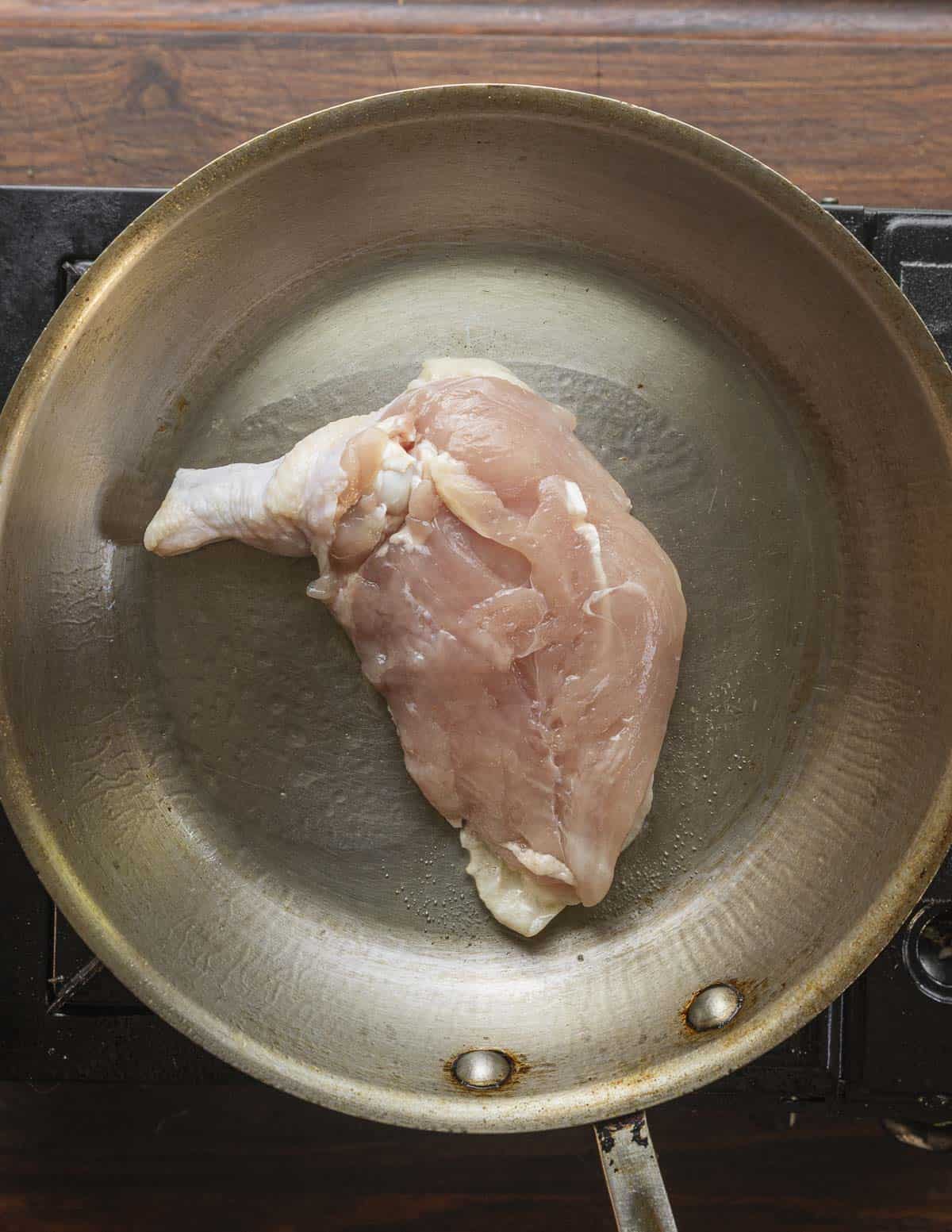 Searing the skin of a bone-in chicken breast in a stainless steel all clad pan. 