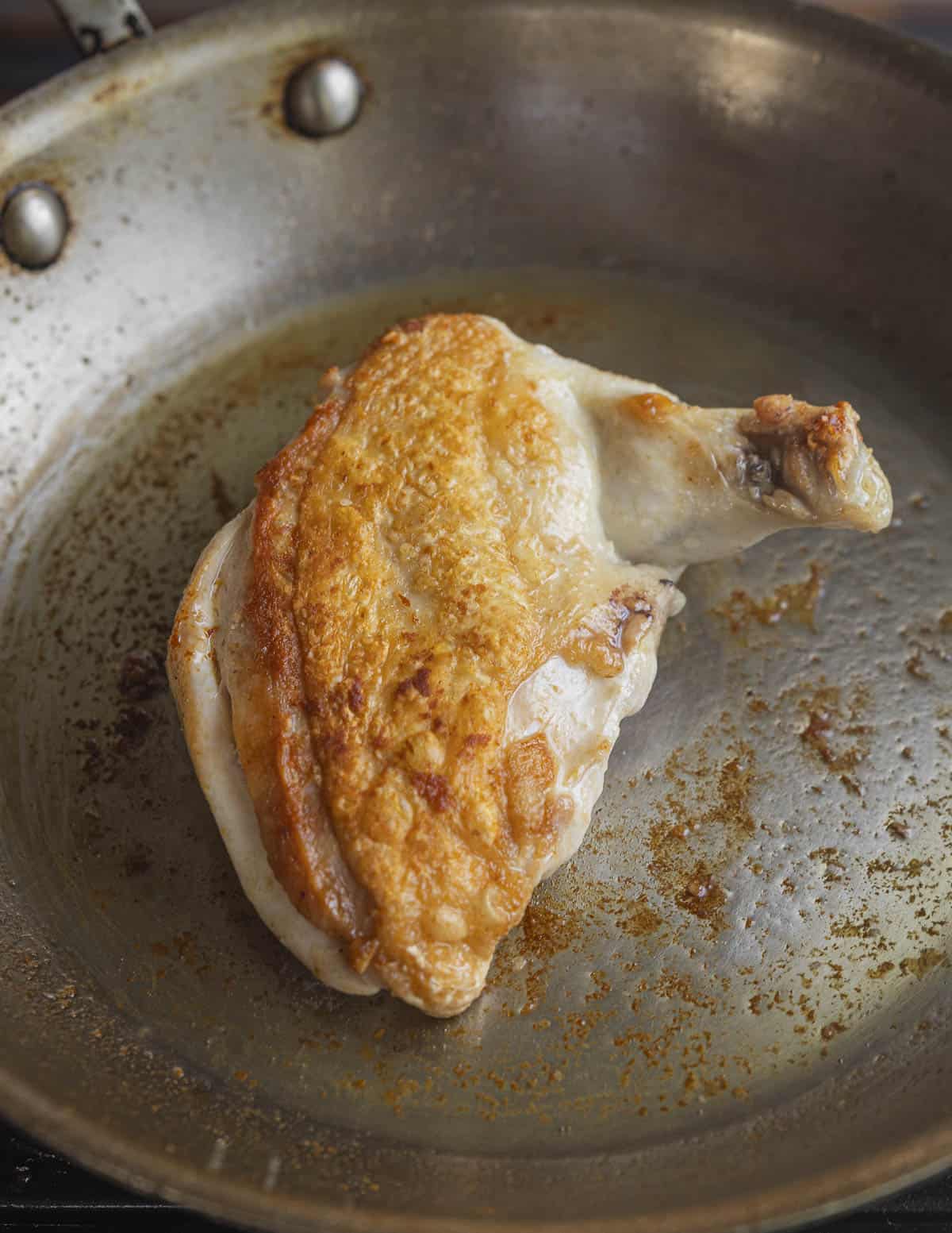 A perfectly golden brown skin on chicken breast in a saute pan ready to rest. 