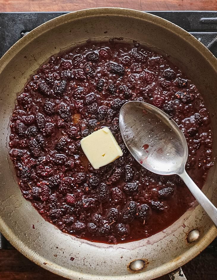 Adding unsalted butter to a pan of mulberry sauce to thicken it. 