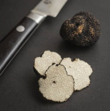 Summer truffles (Tuber aestivum) cut showing the inner white gleba next to a knife and whole summer truffle.