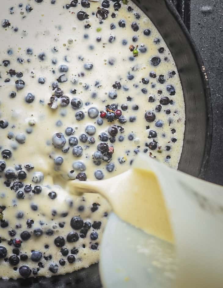 Pouring the rest of the batter over blueberries in a pan to make clafoutis. 