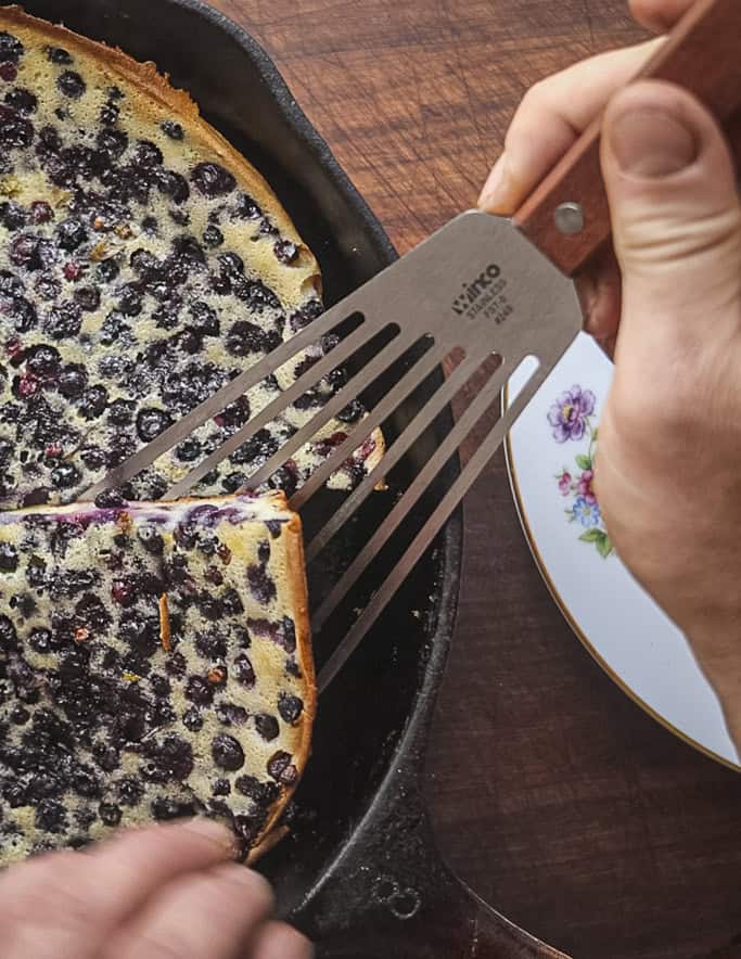 Cutting out a slice of blueberry clafoutis with a spatula. 